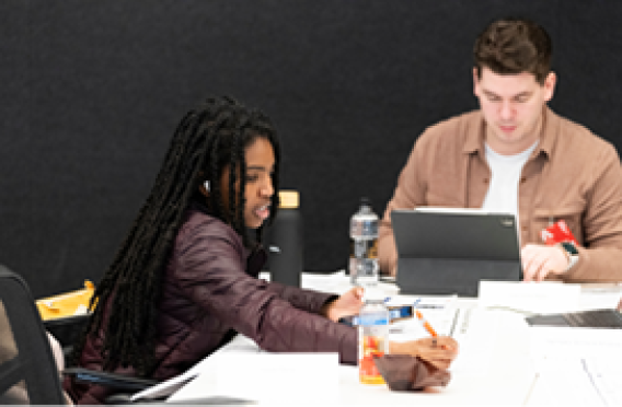 Two people working with paper and tablet at table.