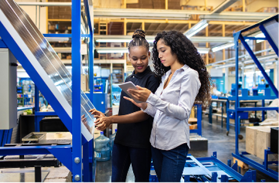 Two professionals using tablet and machinery in advanced manufacturing environment.