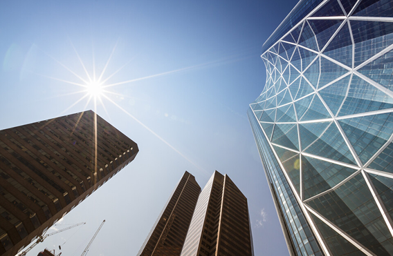 Low-angle view of tall buildings with construction crane and sunburst effect