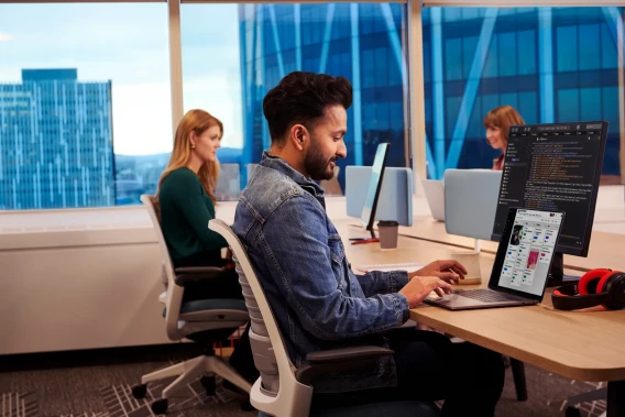 Developer working on a laptop showing code and a product interface in a modern office.