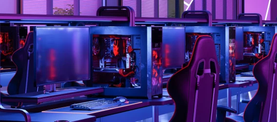 Row of empty gaming stations with monitors and illuminated PCs in a neon-lit esports space.