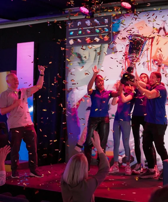 Team celebrating on stage with a trophy as confetti falls during an esports event.