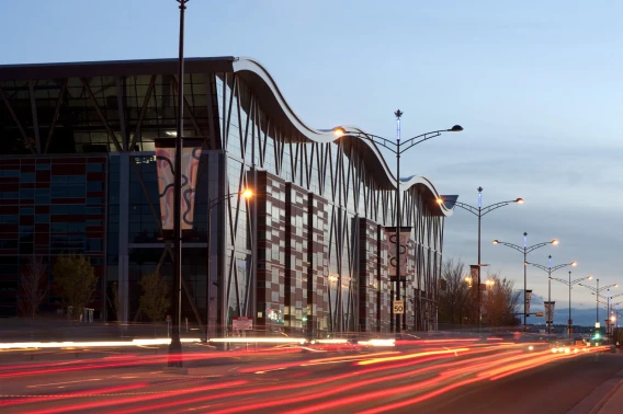 Modern commercial building with a curved roofline and light trails from traffic on the street at dusk.