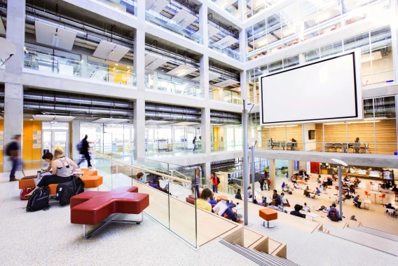 Modern campus atrium with open seating, multiple floors, and students gathered throughout the space.