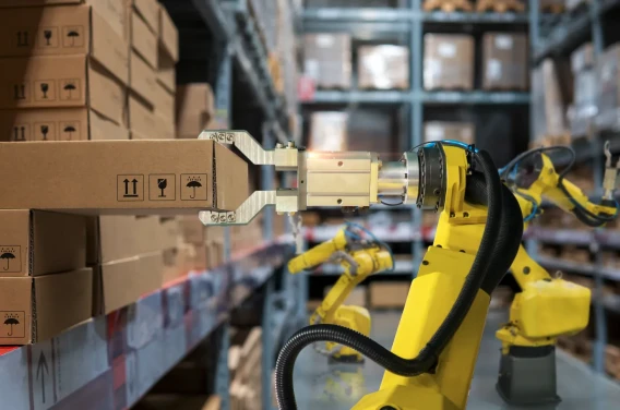 Industrial robotic arm moving cardboard boxes on warehouse shelving.