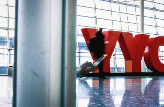 Traveler pulling a suitcase past a large red YYC letter installation inside a bright airport terminal.