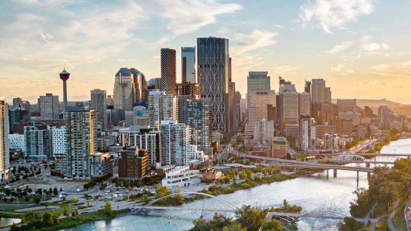 Downtown Calgary skyline at sunset with the Bow River and bridges in the foreground.