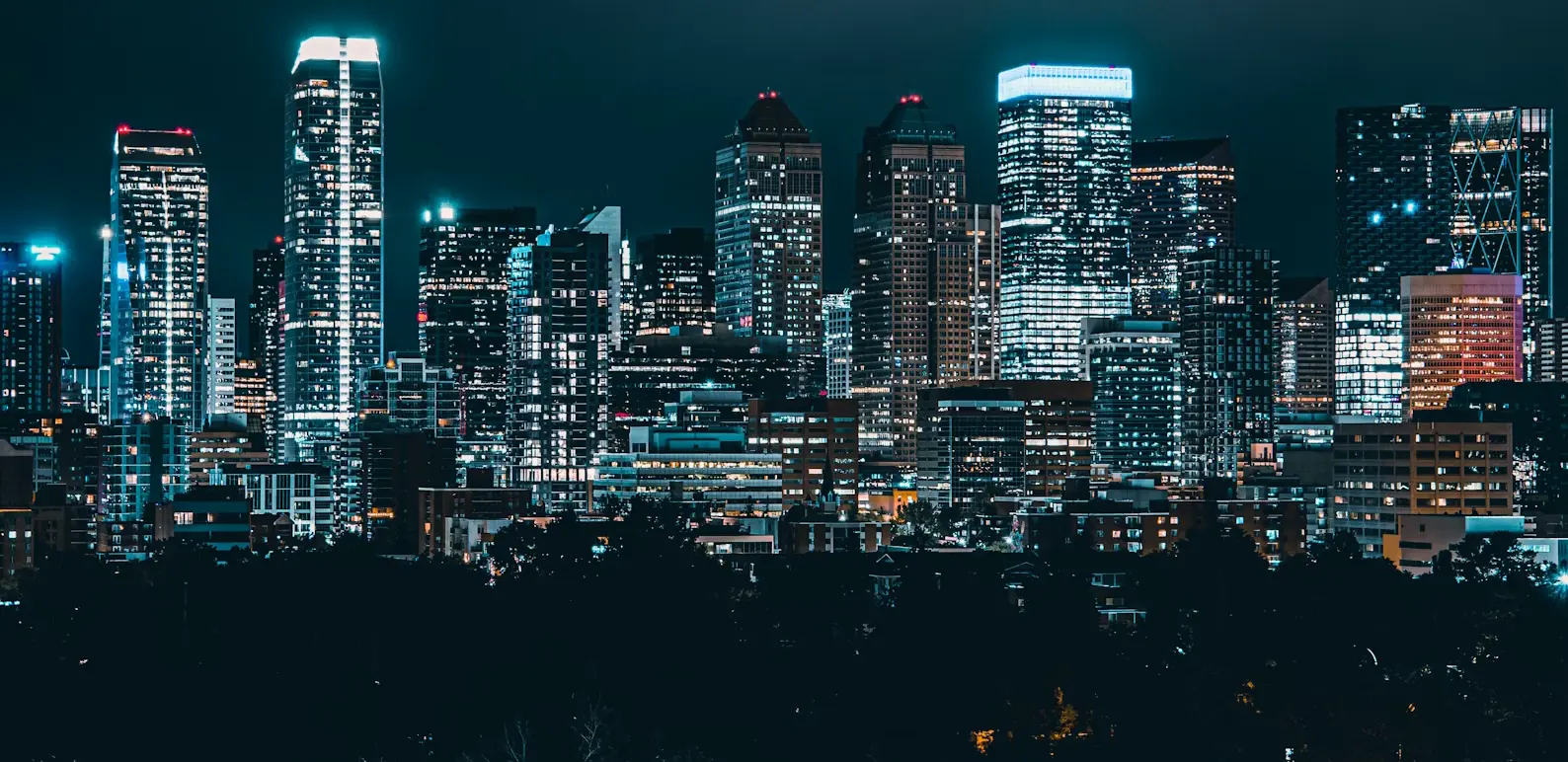 Calgary skyline at night with illuminated downtown skyscrapers against a dark blue sky.