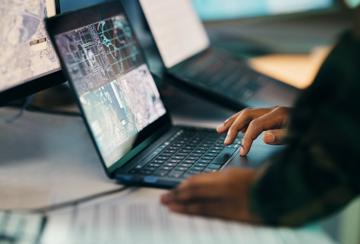 Hands typing, laptop and closeup on table of military intelligence, map and research on internet