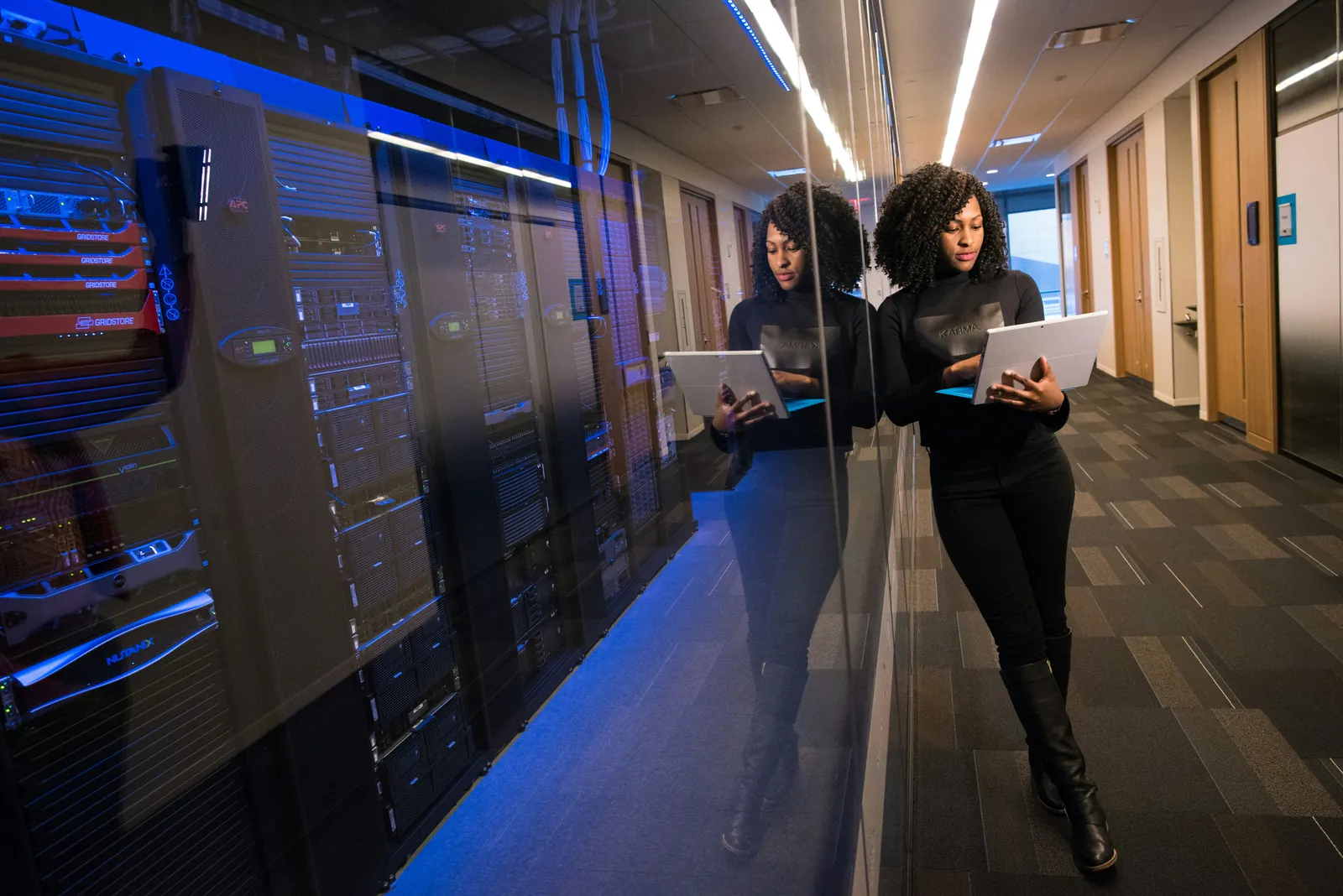 IT professional holding a tablet beside server racks in a data center corridor.