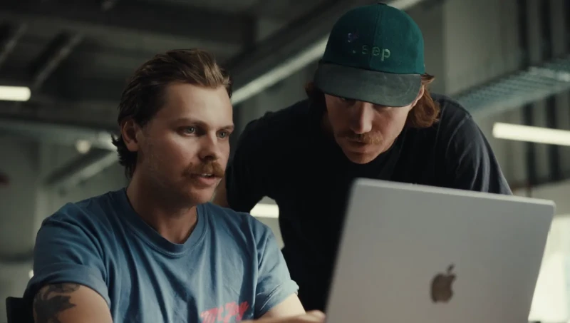 Two team members leaning over a laptop and reviewing work together in an office.